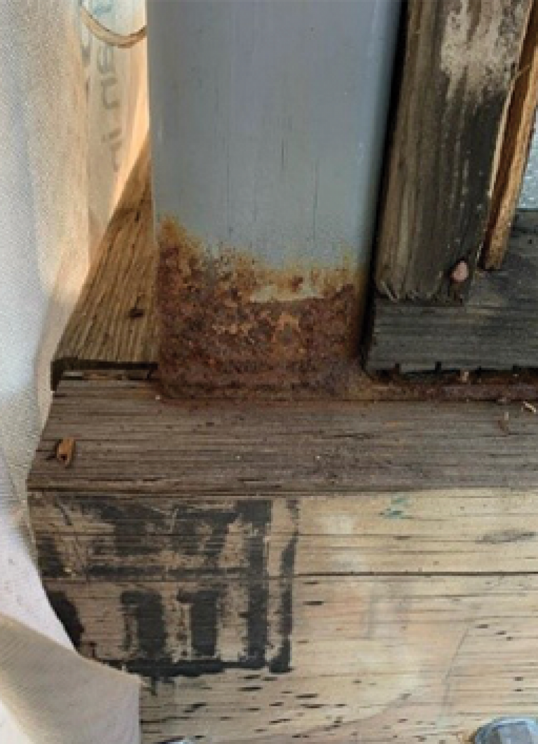 Close-up of rust corrosion at the base of a steel structural post where it meets a timber frame, showing signs of moisture exposure and deterioration.