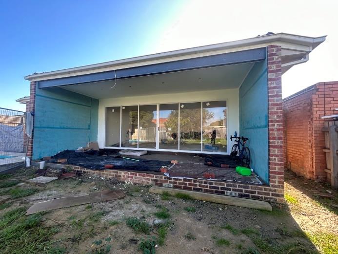 Rear patio of a single‑storey house under construction with sliding glass doors and exposed groundwork.