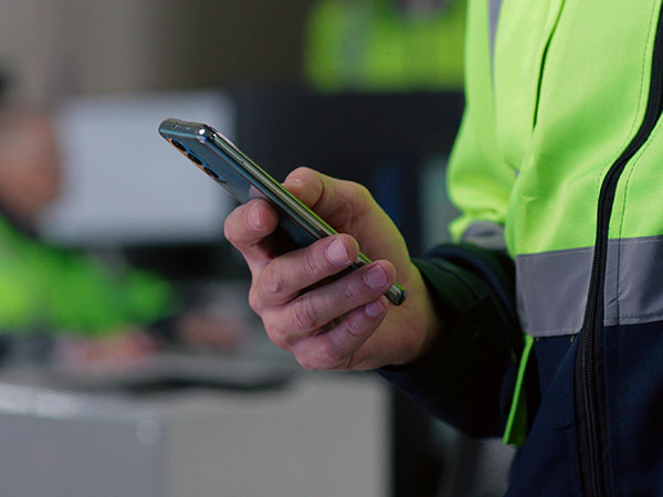 Hand holding a smartphone while wearing a high-visibility work jacket with reflective striping.