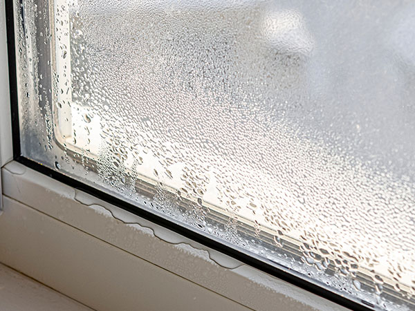 Close-up of a window with heavy condensation and water droplets covering the glass, with moisture collecting along the frame at the bottom.