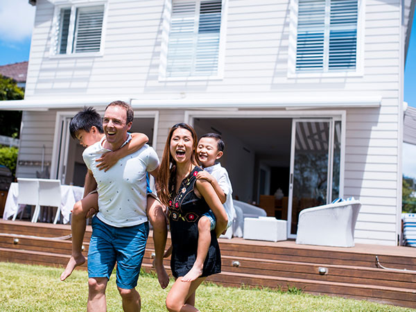 Family carrying children on their backs while walking on a lawn in front of a modern house.