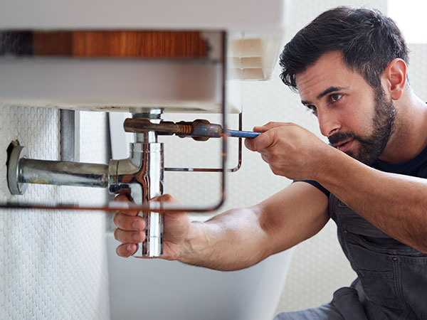 Person tightening pipes under a sink with a wrench.