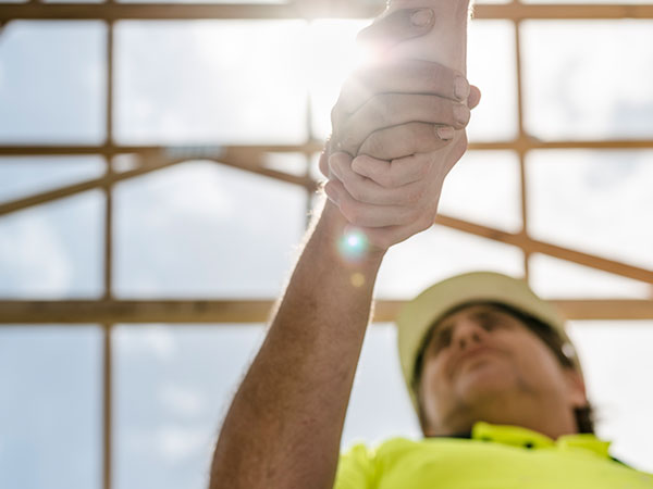 Close-up of two hands clasped together, with a construction worker in a hi-vis shirt and hard hat blurred in the background.