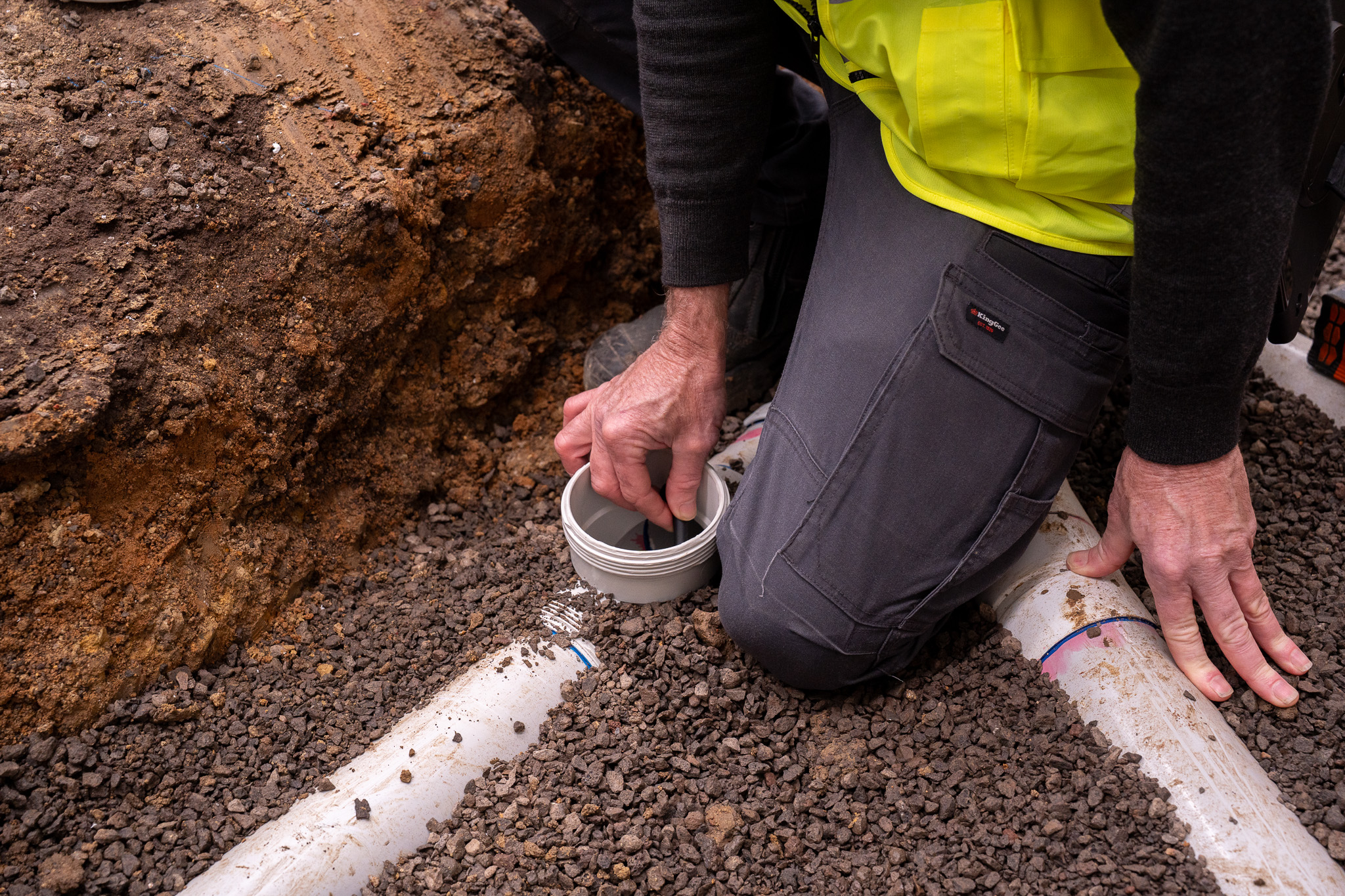 The hand of an inspector is near a drain pipe in the ground