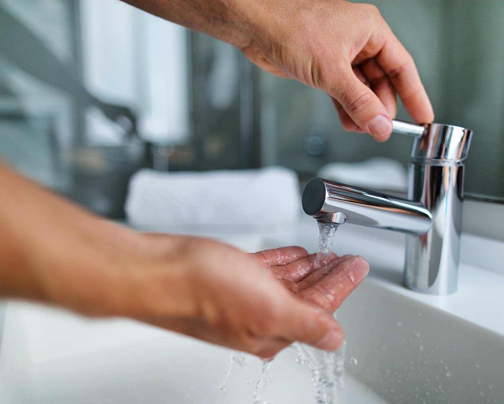A pair of hand turning on a tap and feeling the water